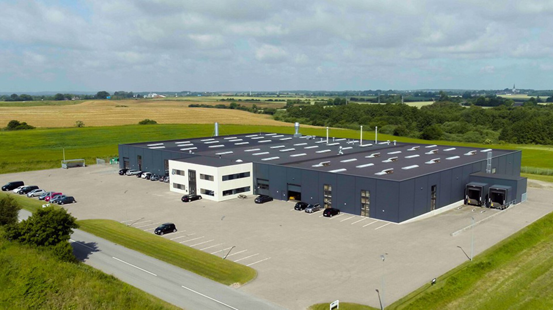 LINAK Profiles - aerial view of a modern industrial building with white and dark facades, parking areas, and surrounding green fields.