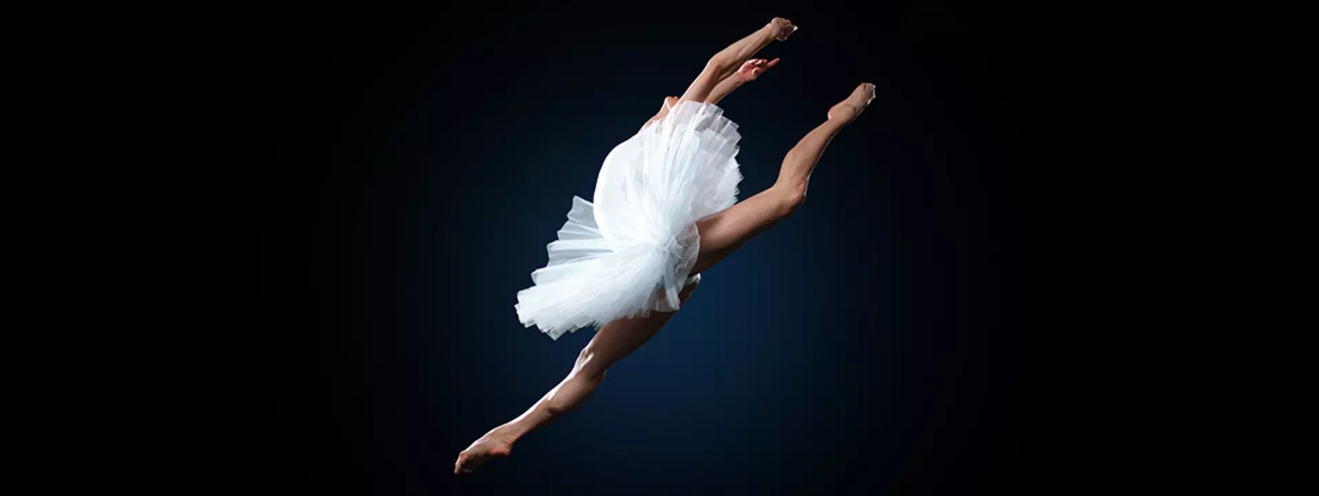 Ballerina posing with arms raised, wearing a red dress, water splashing on her. Black background.