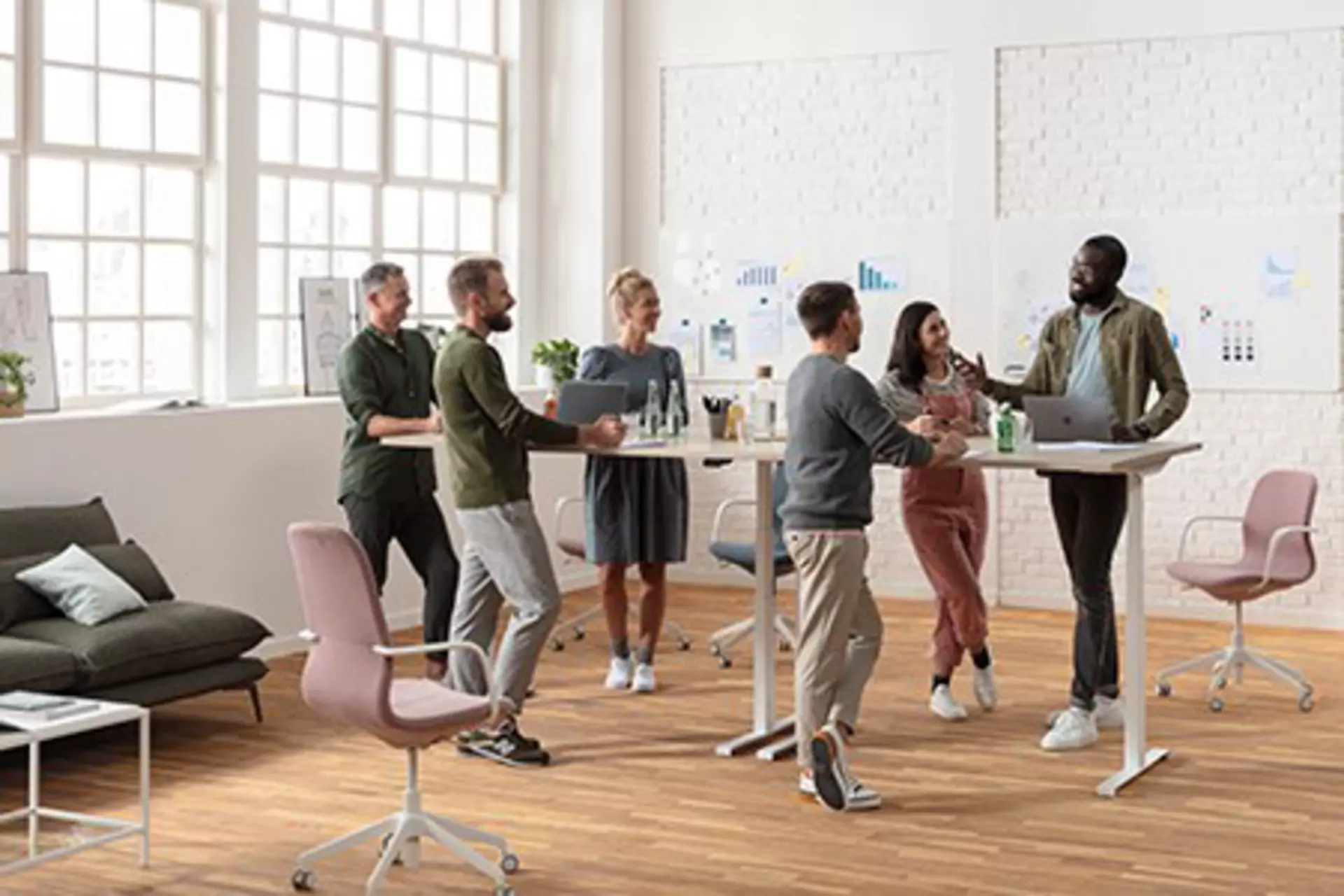 Office workers standing at an ergonomic and adjustable conference desk.