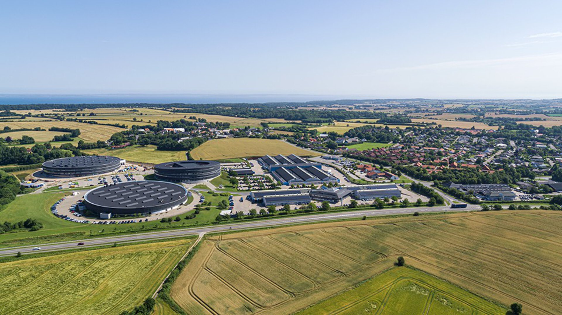 Aerial view of LINAK headquarters - a large manufacturing site with multiple buildings, parking areas, and green farmland around it.
