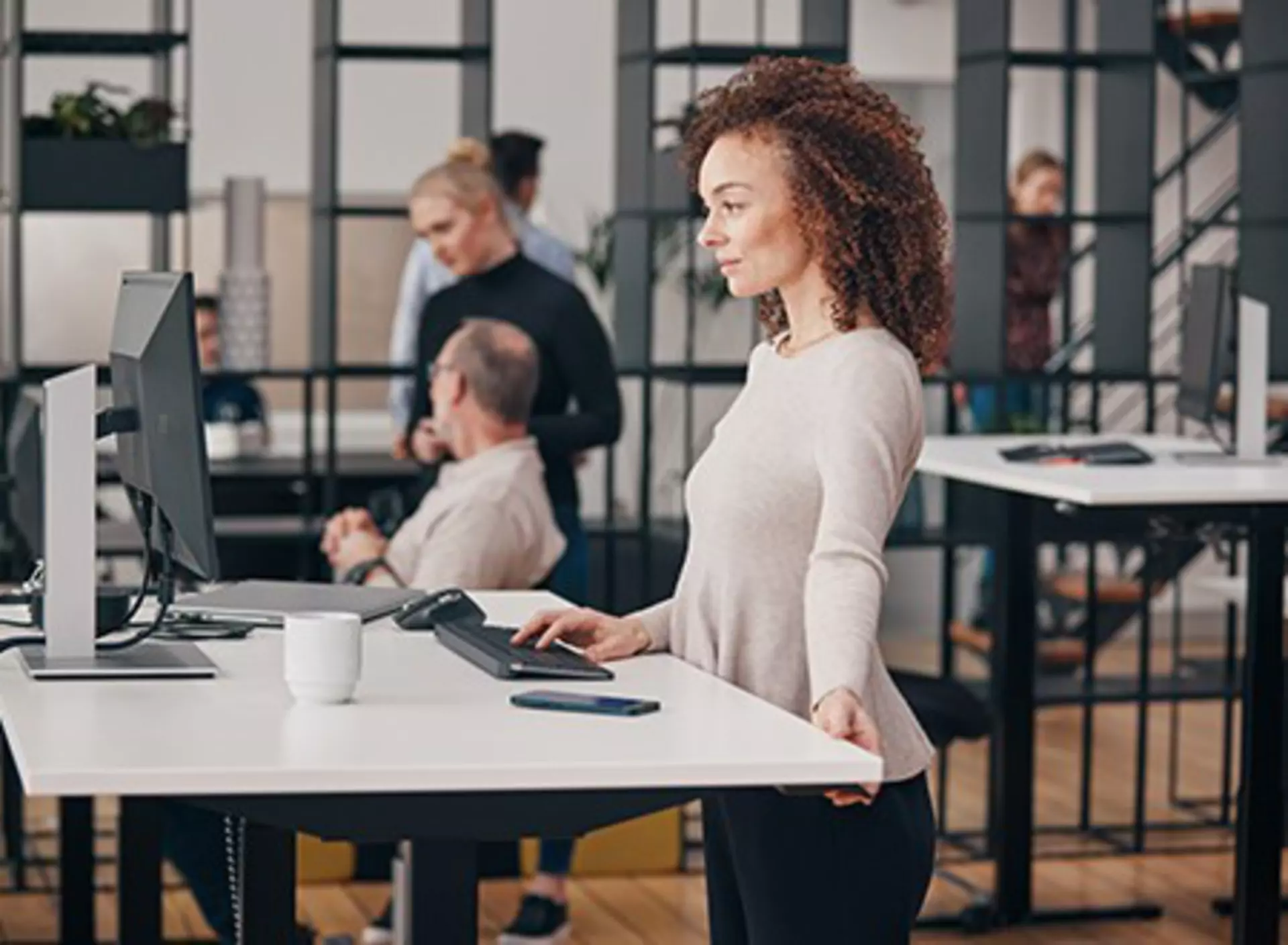 Woman adjusting her office desk with the intuitive desk control, colleagues in the background
