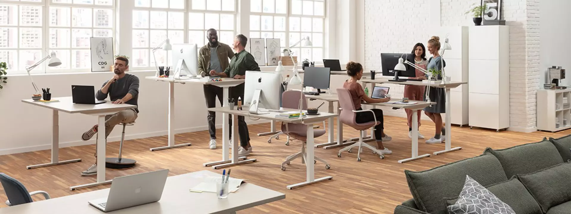 Office workers standing and sitting at ergonomic and adjustable office desks in a modern office