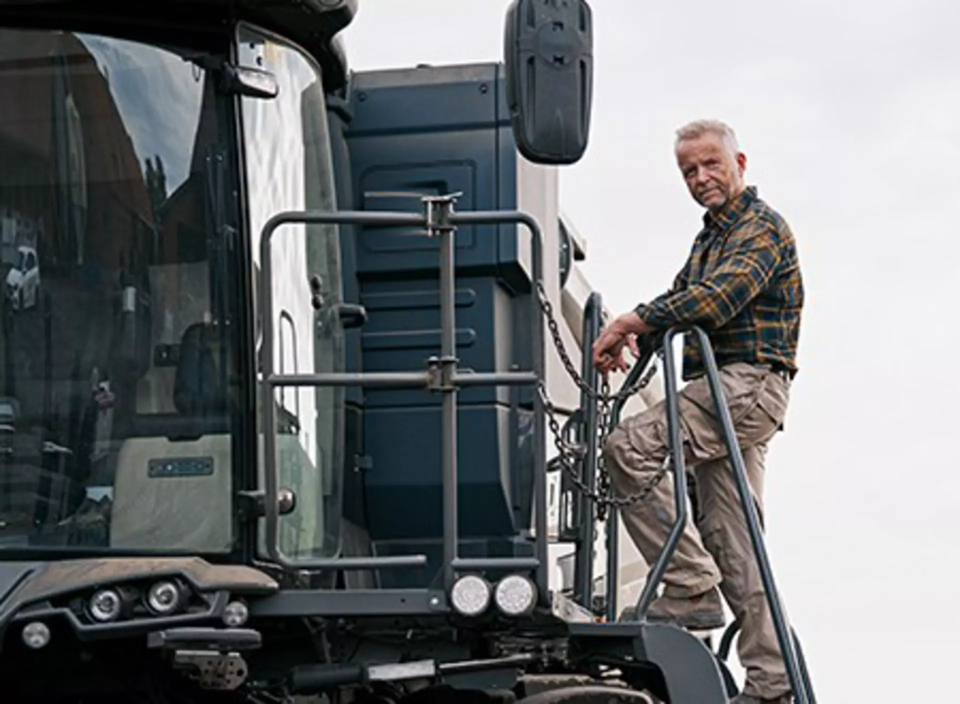 Elderly farmer climbs the ladder to enter the operator cab of a big agricultural machine