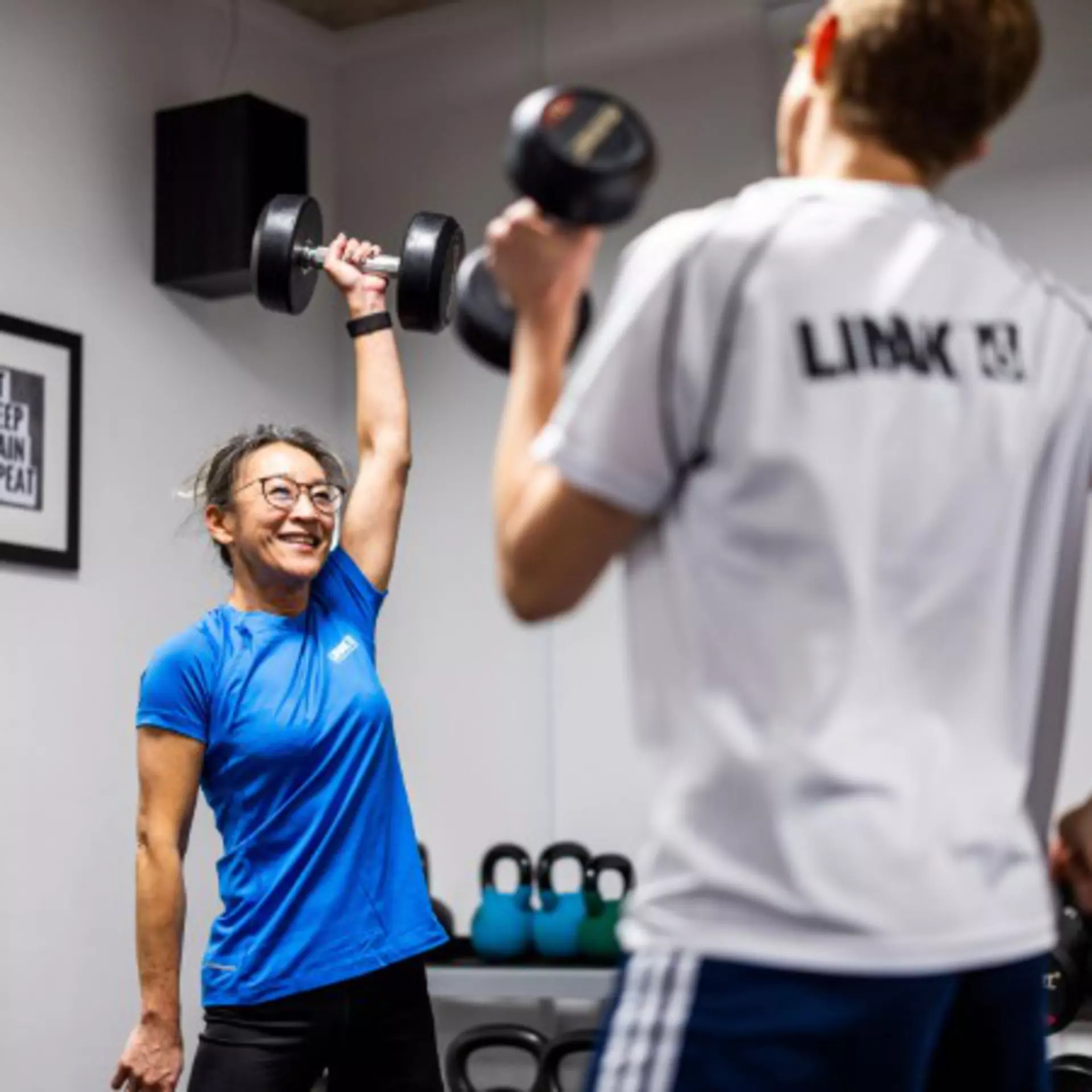 LINAK employees exercising in the LINAK fitness room, lifting dumbbells.