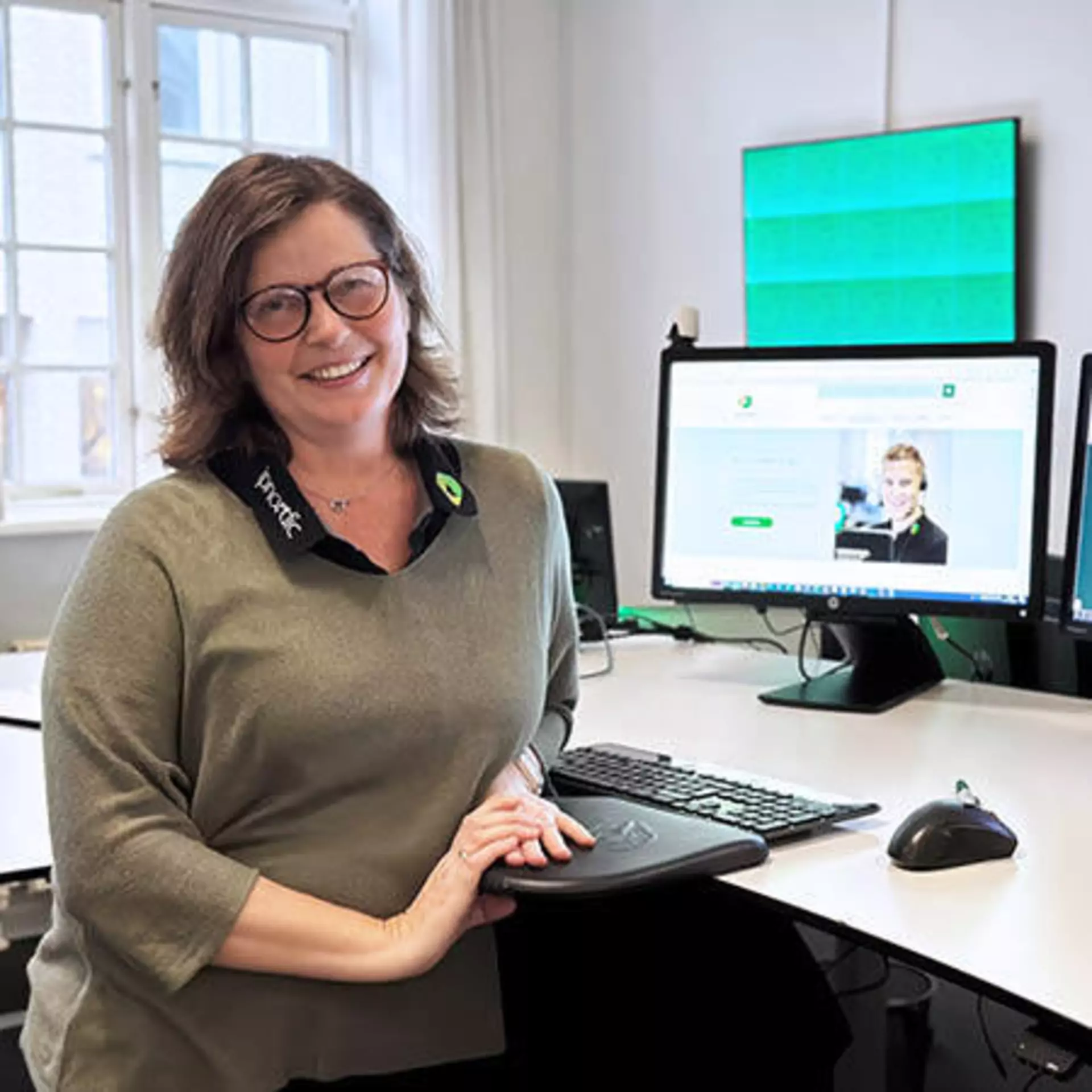 Smiling ipnordic employee standing at her sit-stand desk with a computer in the background