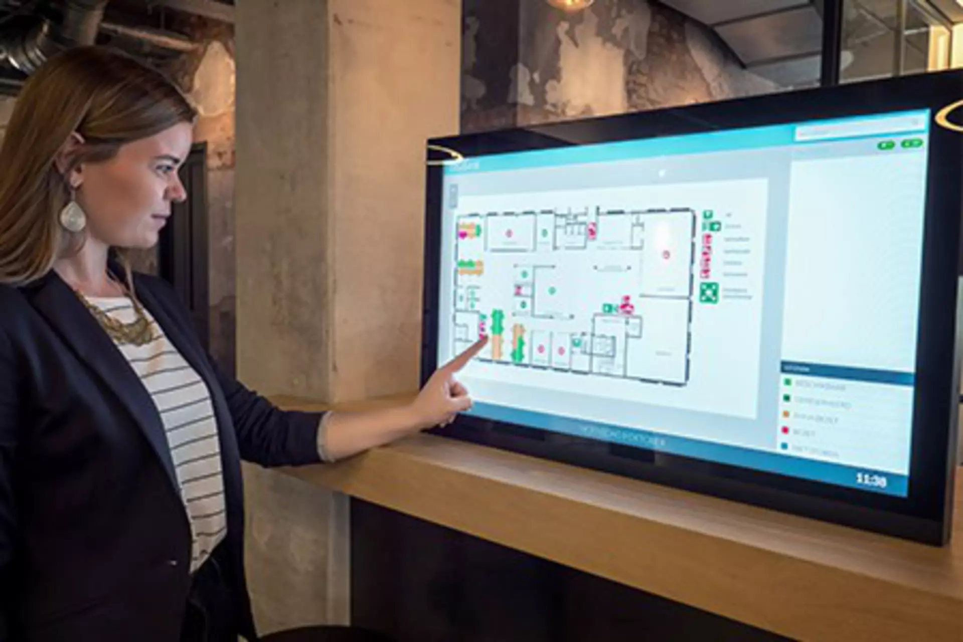 Young, female office worker booking an office desk at touch screen in an office – activity based working.