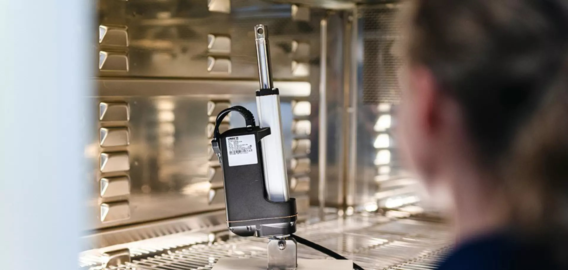 A person observing a LINAK linear actuator inside a high-tech testing chamber, showcasing precision engineering and quality control