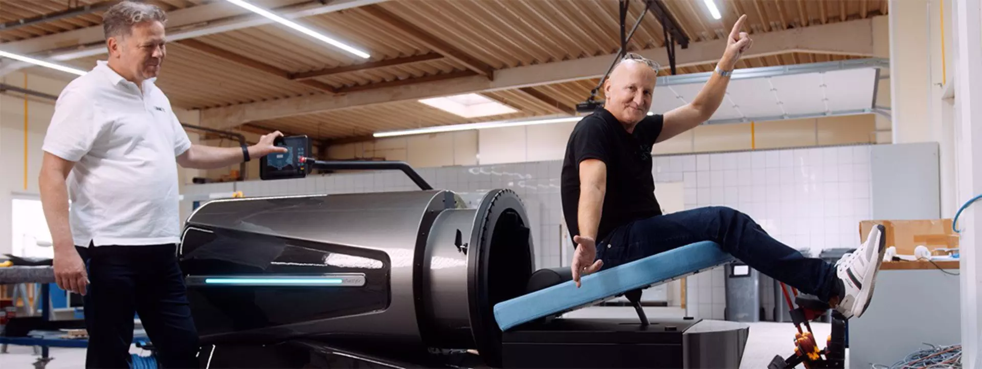 Smiling man sitting on actuator-raised blue headrest. Man stands next to Flow capsule.