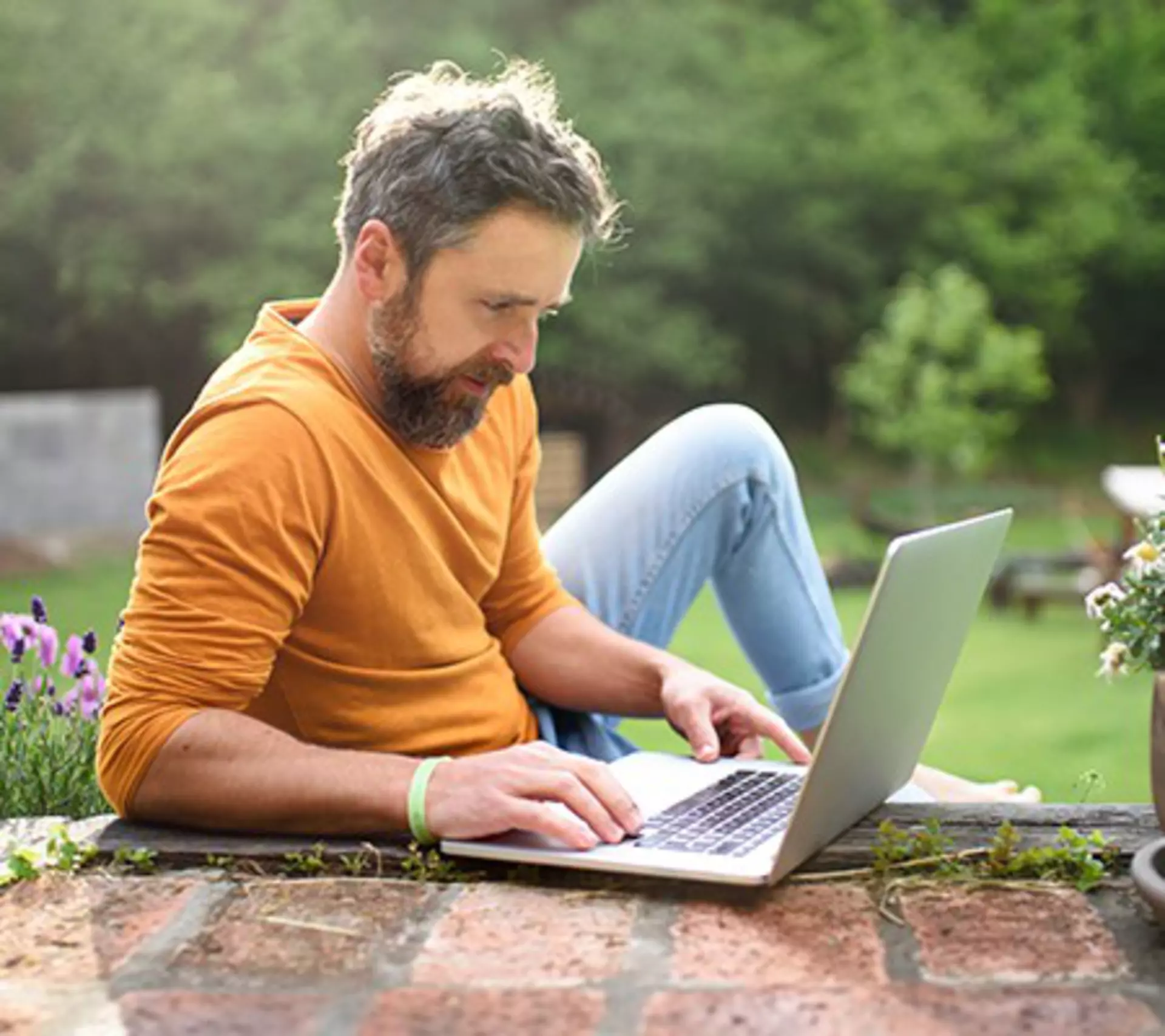 Young man with laptop working from home from his garden.